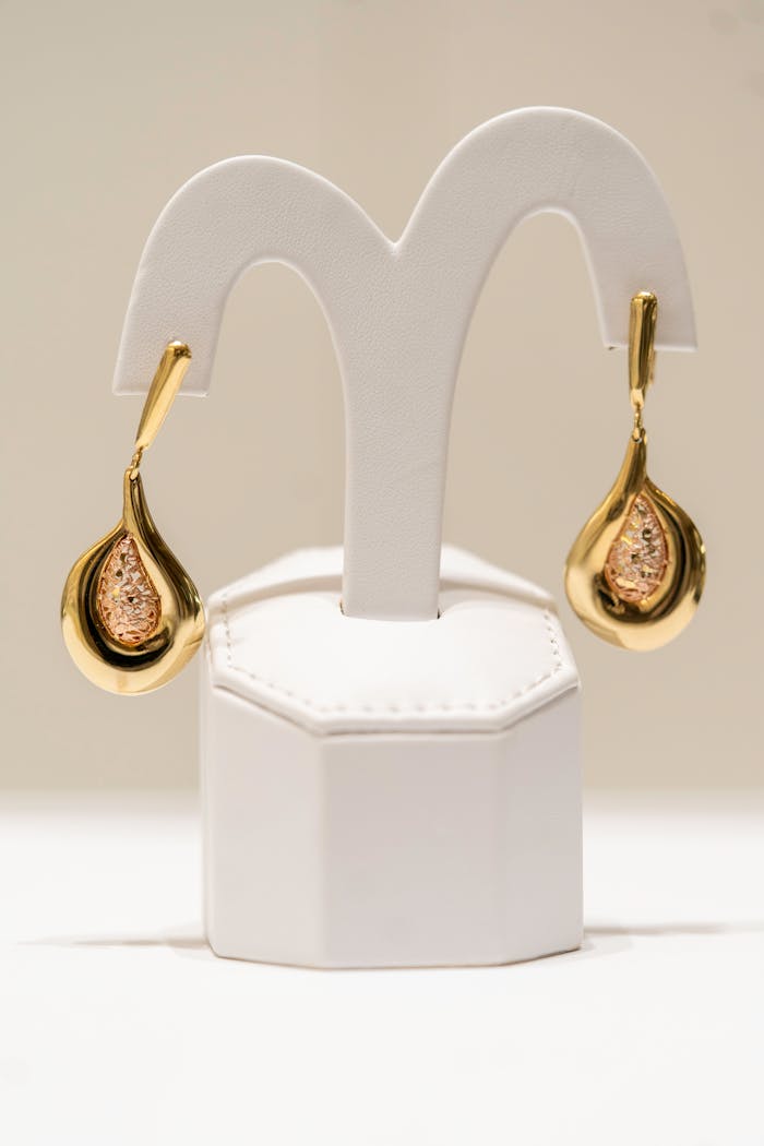 Luxurious gold earrings beautifully displayed on a white stand in a well-lit environment.